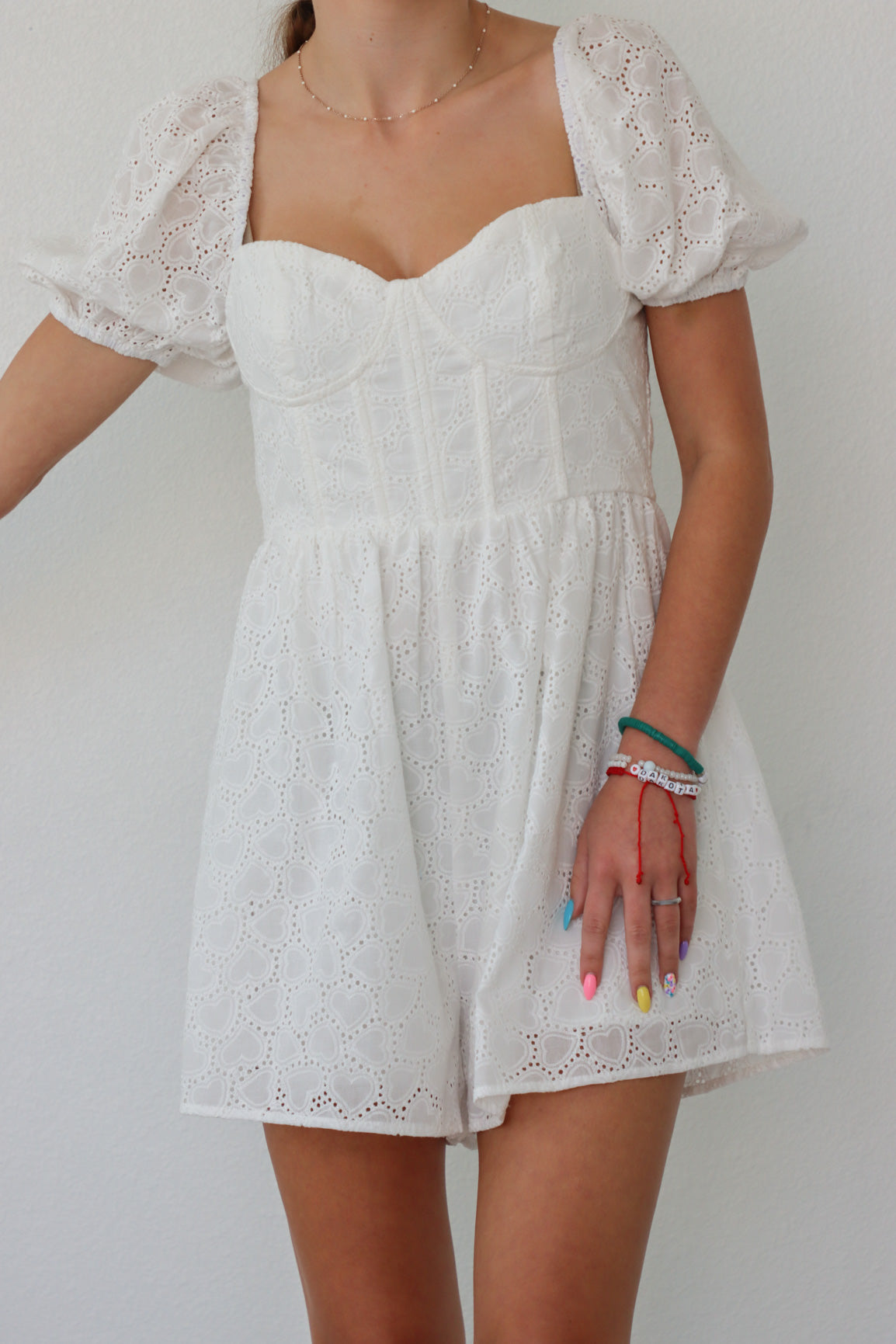 girl wearing white romper with puff sleeves and heart eyelet fabric