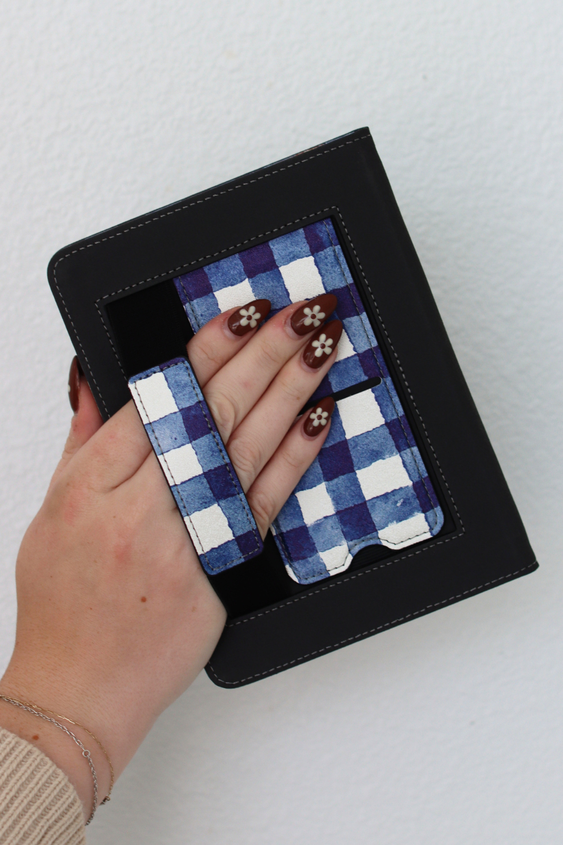 Hand holding a black Kindle with a blue and white checkered pattern and a hand inside.