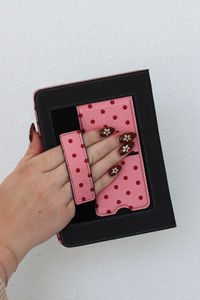 Hand holding a black kindle case with a pink polka dot pattern on a white background