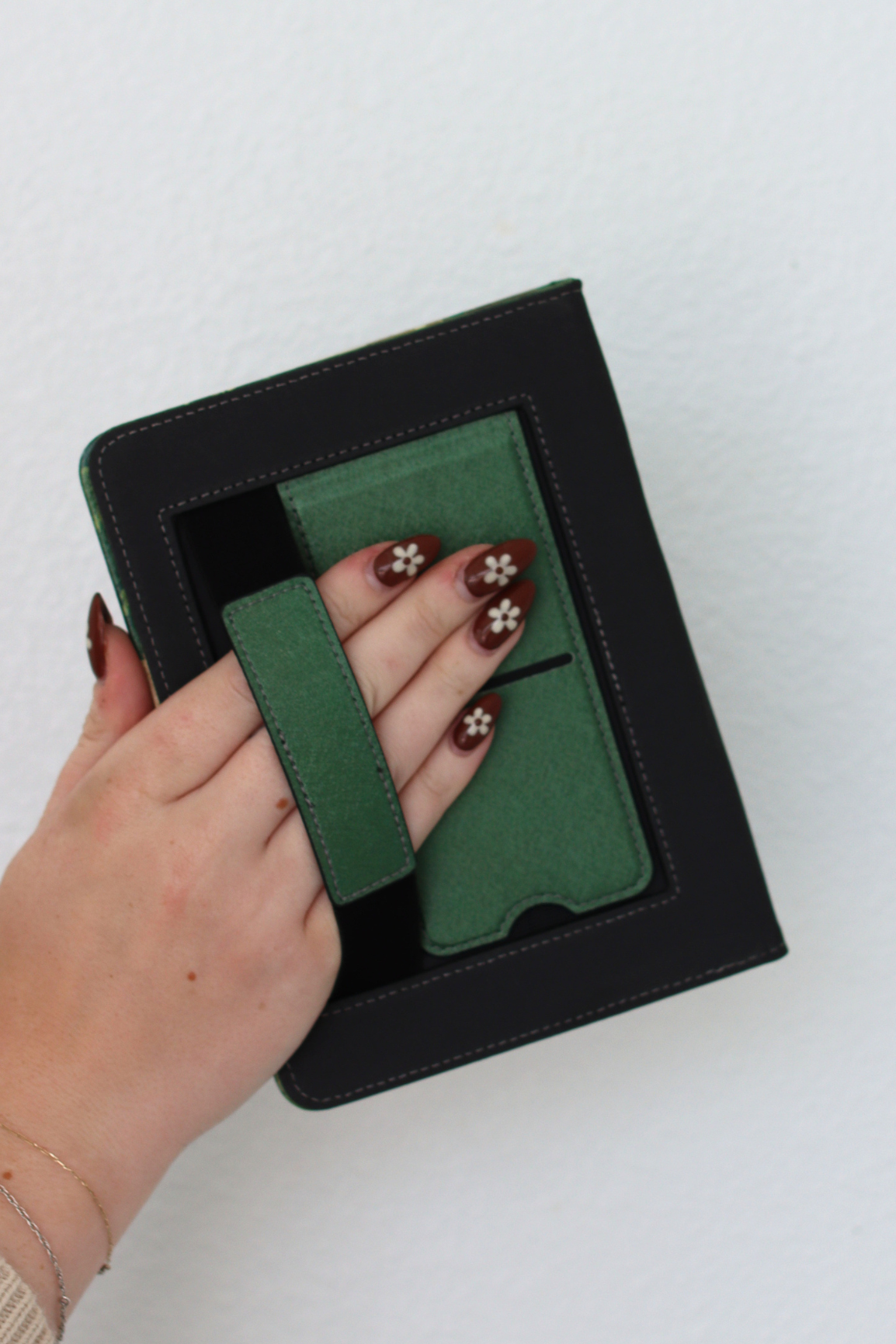 Hand holding a green kindle case with floral designs against a white background
