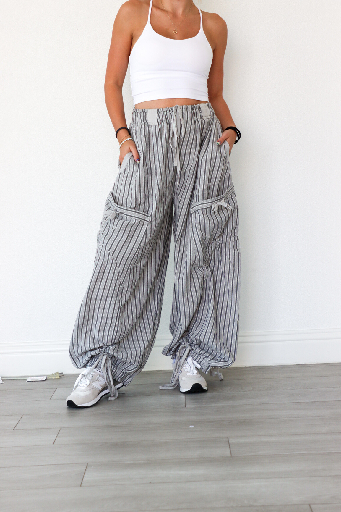 Person wearing a white tank top and striped wide-leg pants against a white wall.