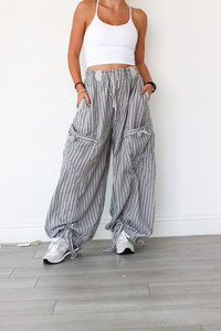 Person wearing a white tank top and striped wide-leg pants against a white wall.