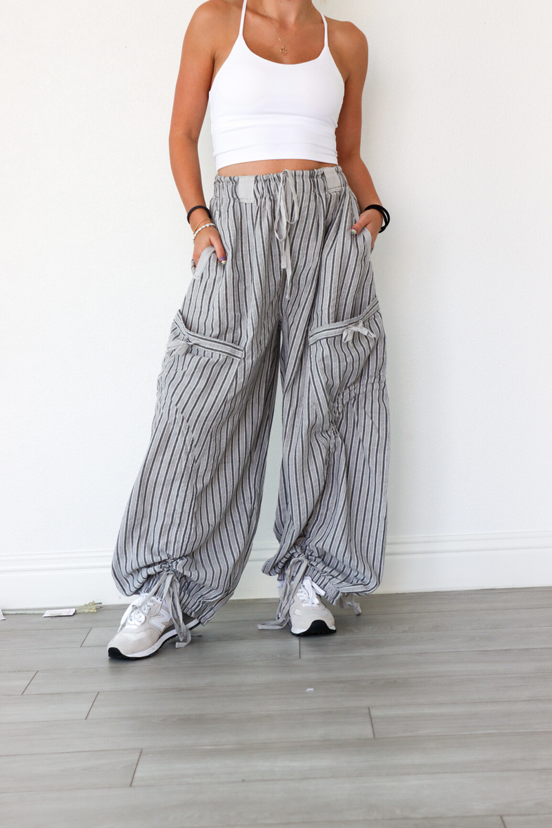 Person wearing a white tank top and striped wide-leg pants against a white wall.