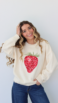Woman wearing a cream sweater with a strawberry design against a white background