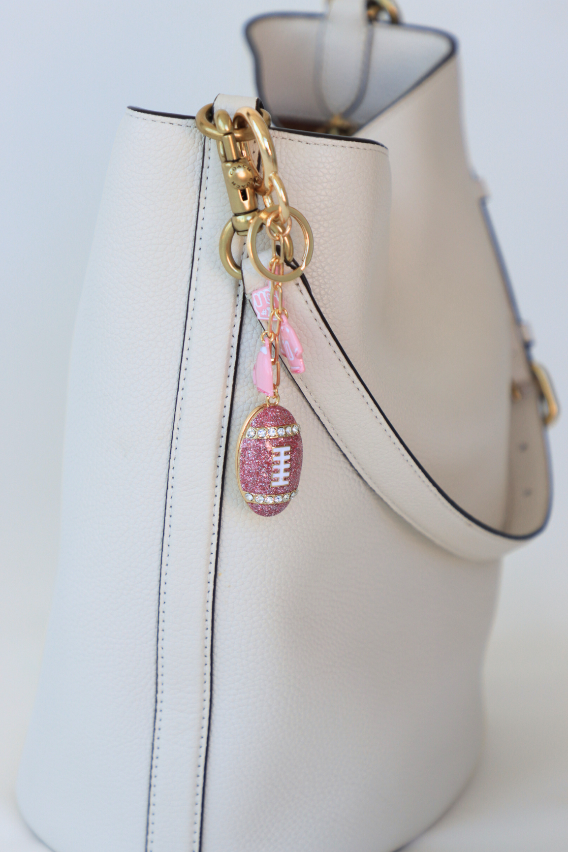 Pink glittery football keychain attached to a white handbag.