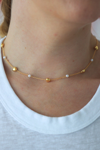 Gold necklace with small beads worn by a person on a white background
