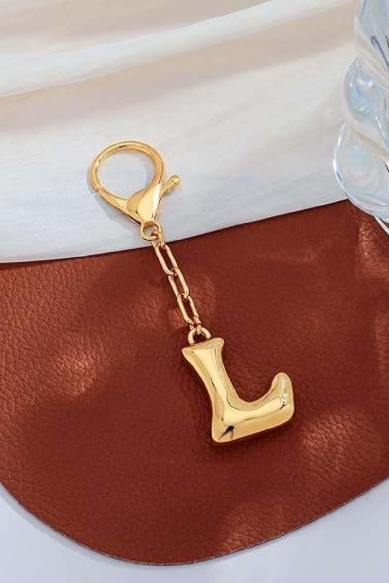 Gold letter 'L' keychain on a brown leather surface