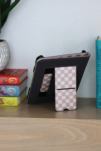 A nook case with a purple and cream checkerboard patterned front cover, standing on a wooden shelf next to books.