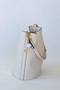 Beige handbag with gold chain and lock charm on a white background