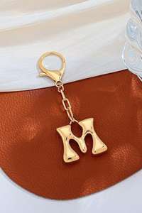 Gold letter 'M' keychain on a brown leather surface