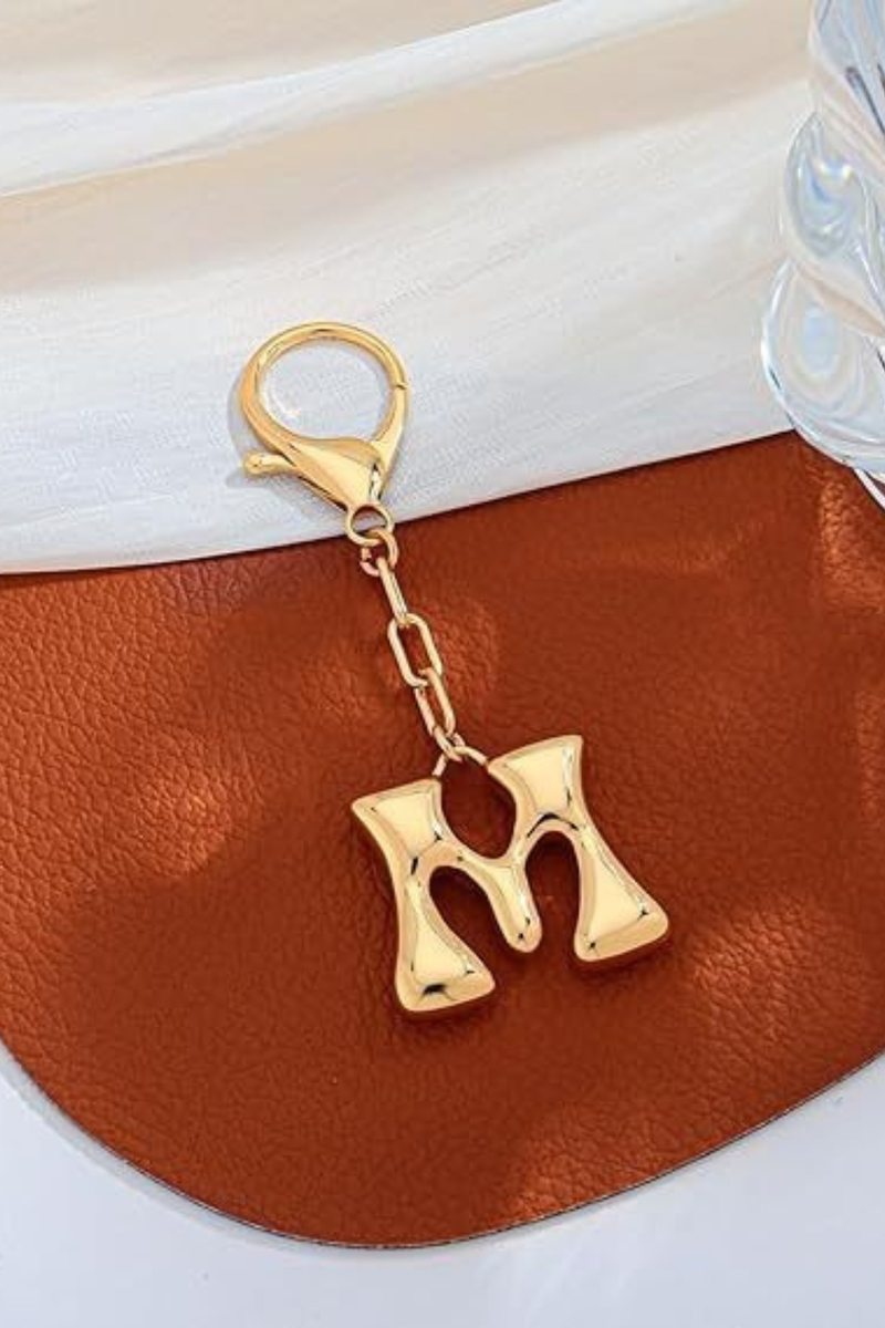 Gold letter 'M' keychain on a brown leather surface
