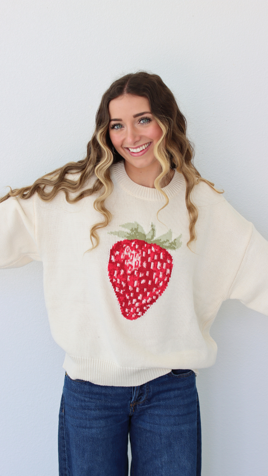 Woman wearing a cream sweater with a strawberry design against a white background