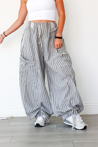 Person wearing gray striped wide-leg pants and white sneakers on a light wooden floor.
