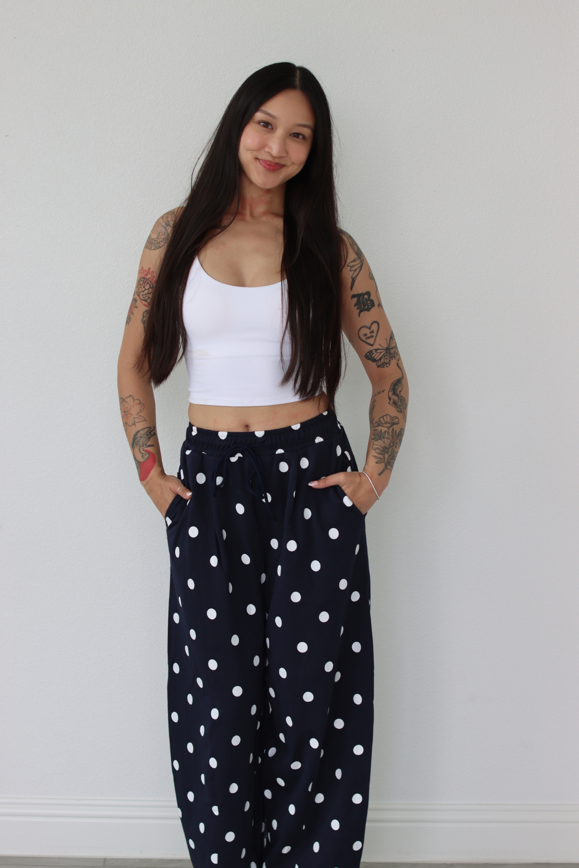Woman wearing a white top and navy polka dot pants against a white wall.