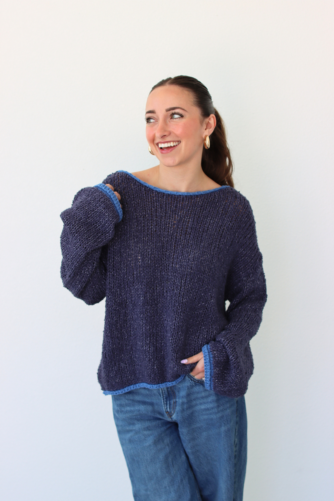 Woman wearing a dark blue sweater and jeans against a white background