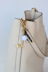 Beige handbag with decorative charm on a light gray background