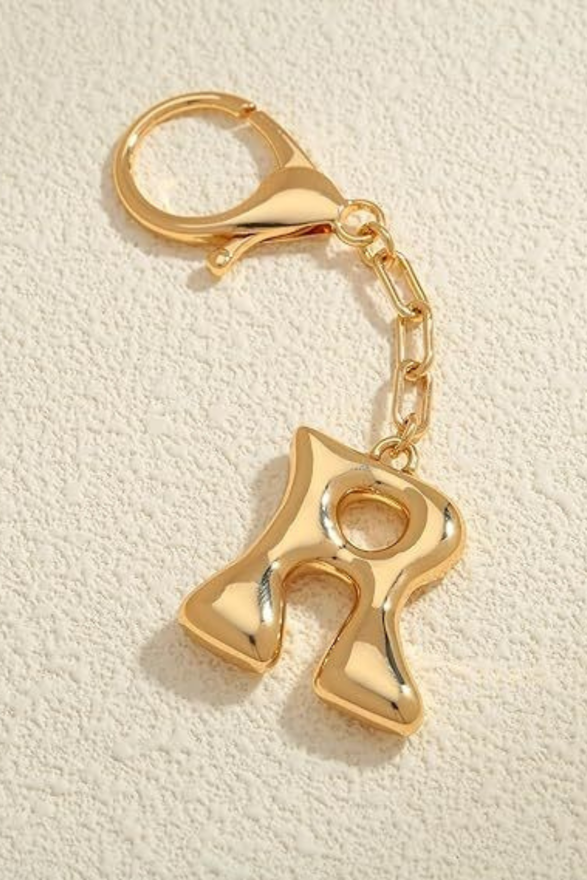 Gold keychain with letter 'R' on a beige background