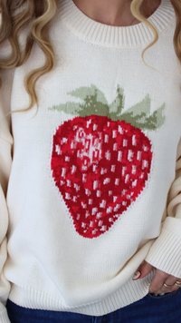 White sweater with a red strawberry design worn by a person.