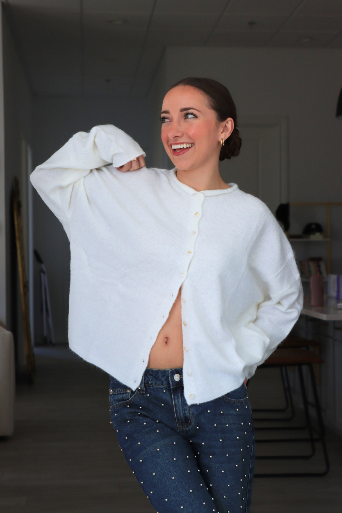 Woman wearing a white sweater and blue jeans indoors