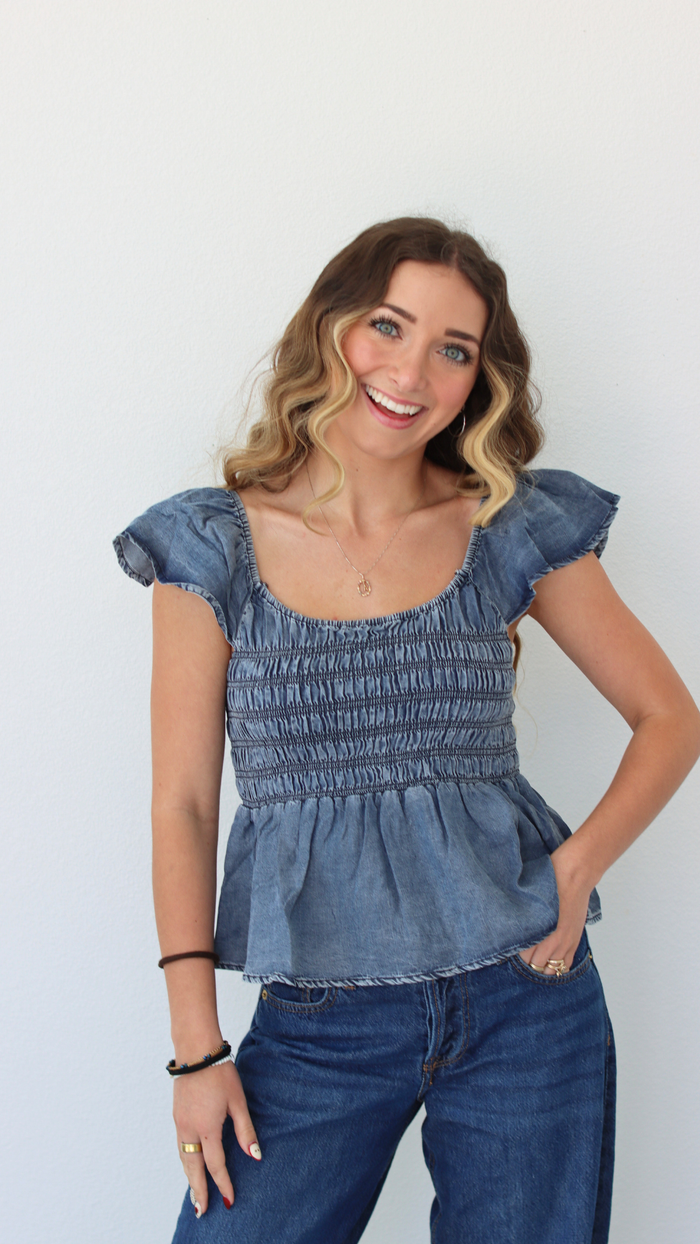 Woman wearing a blue denim top and jeans against a white background