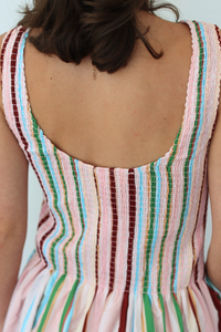 Close-up back view of a person wearing a sleeveless dress with vertical multicolor stripes in pink, green, blue, and burgundy on a light background.