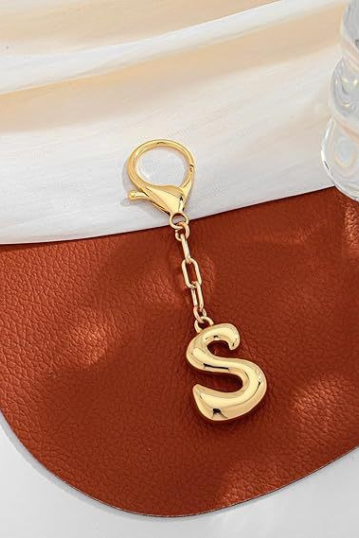 Gold letter 'S' keychain on a brown leather surface