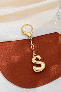 Gold letter 'S' keychain on a brown leather surface