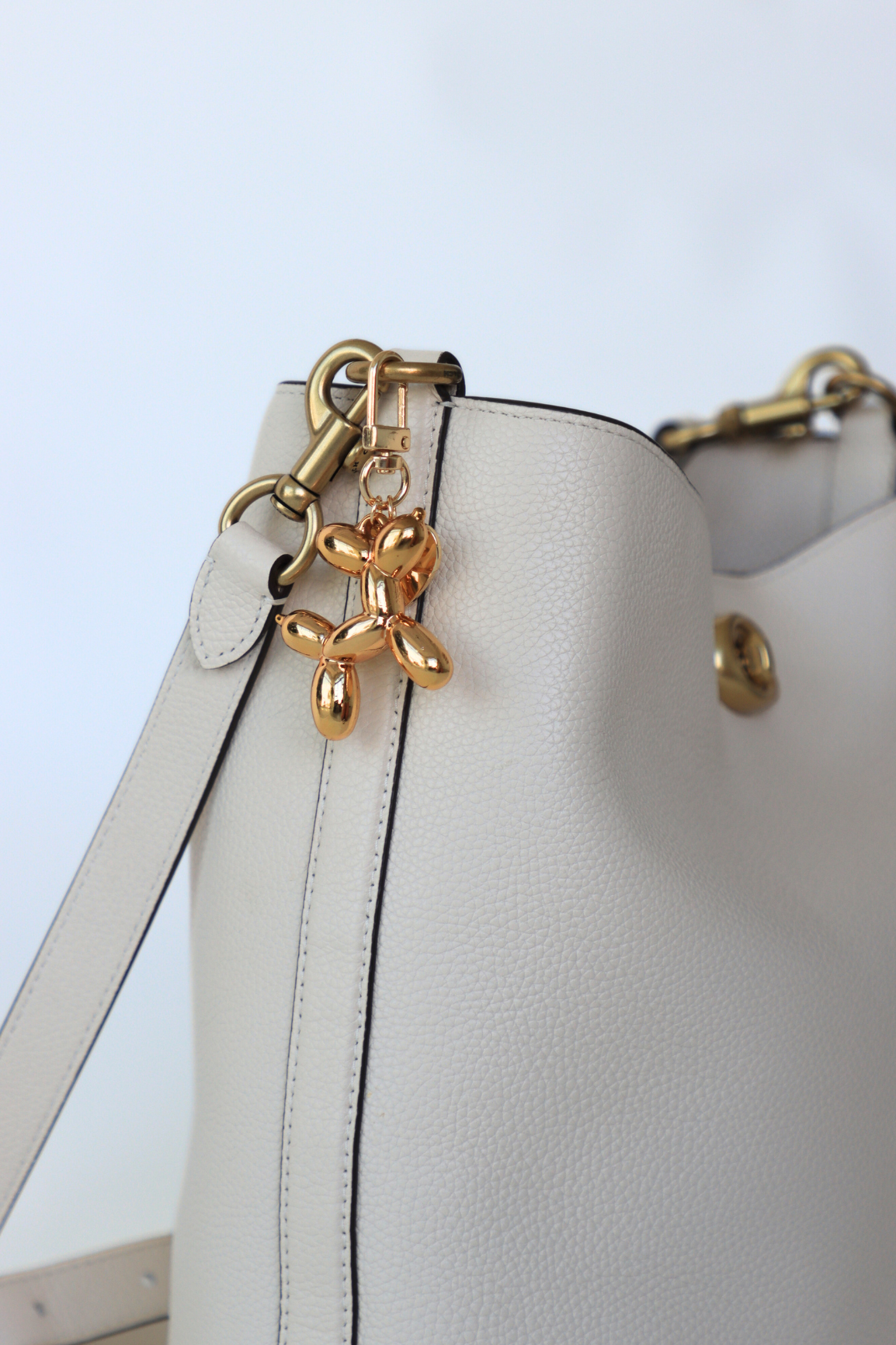 White handbag with gold butterfly charm on a light blue background