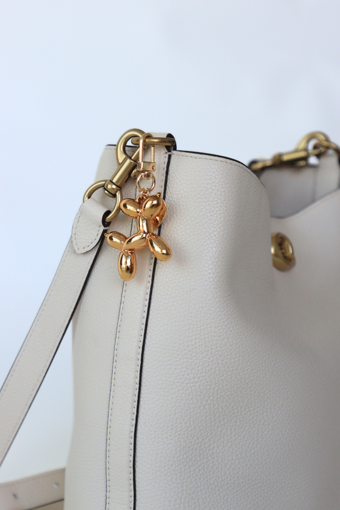 White handbag with gold butterfly charm on a light blue background