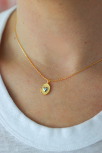 Gold necklace with a heart pendant worn by a person on a white shirt background