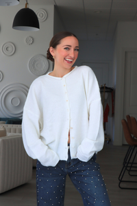 Woman wearing a white cardigan and blue jeans indoors.