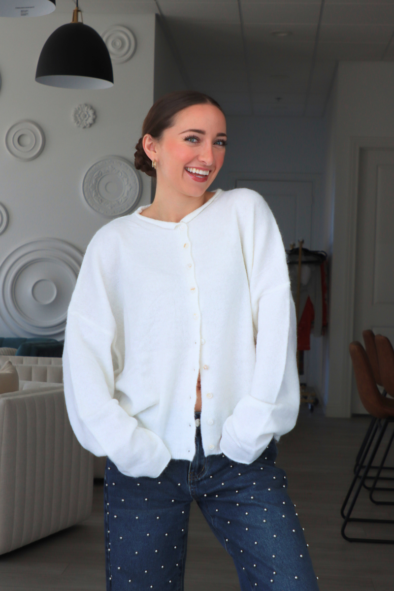 Woman wearing a white cardigan and blue jeans indoors.