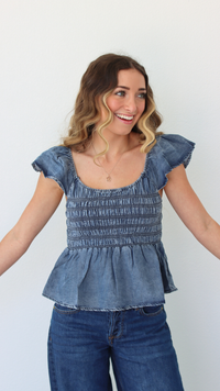 Woman wearing a blue denim top and jeans against a white background
