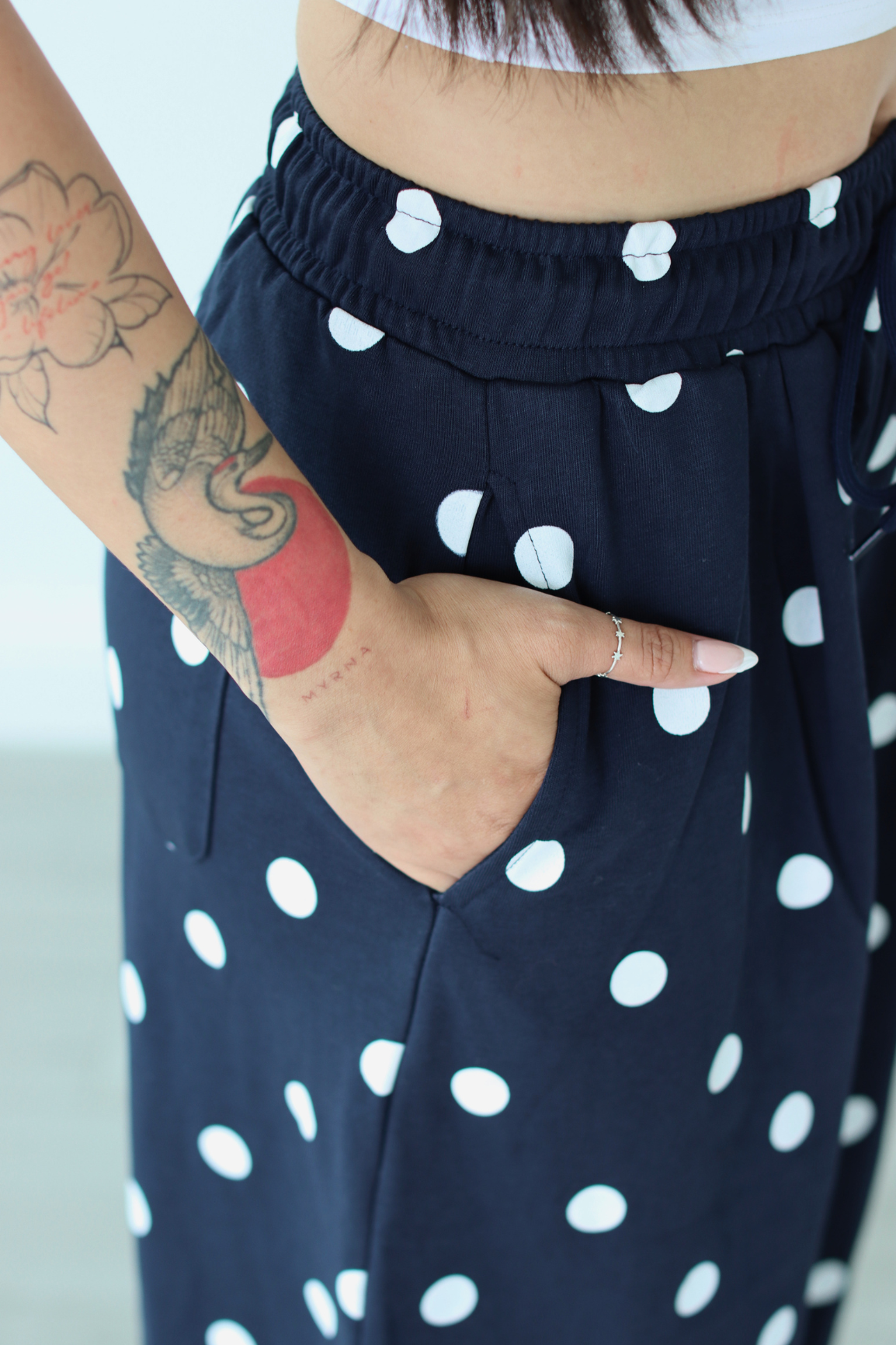 Navy blue pants with white polka dots worn by a person with tattoos on their arm.
