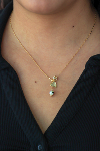 Gold necklace with a heart-shaped pendant worn by a person against a black shirt.