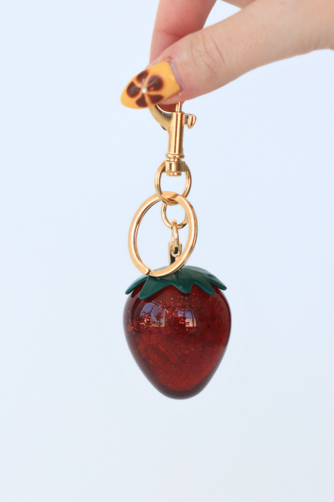Strawberry-shaped keychain with gold clasp on a light blue background