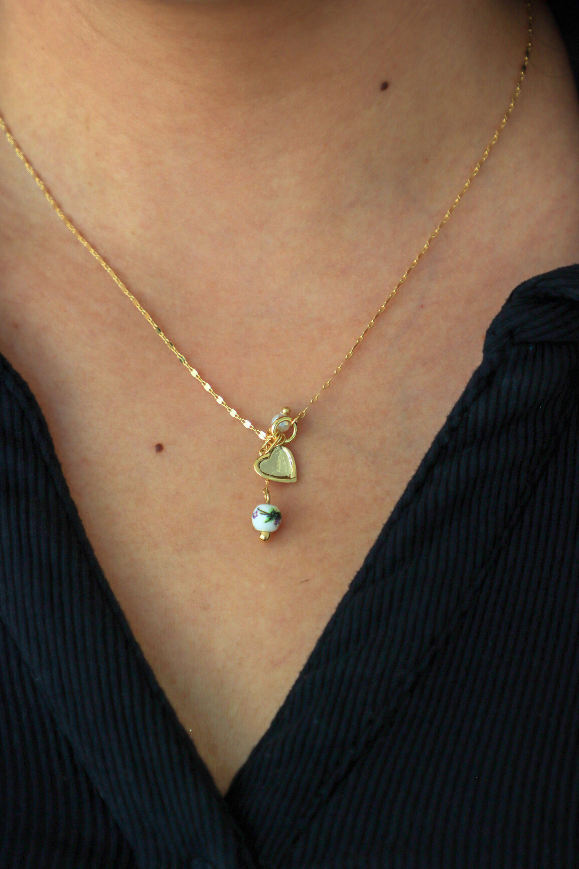 Necklace with a heart-shaped pendant and green gemstone on a person wearing a black top.