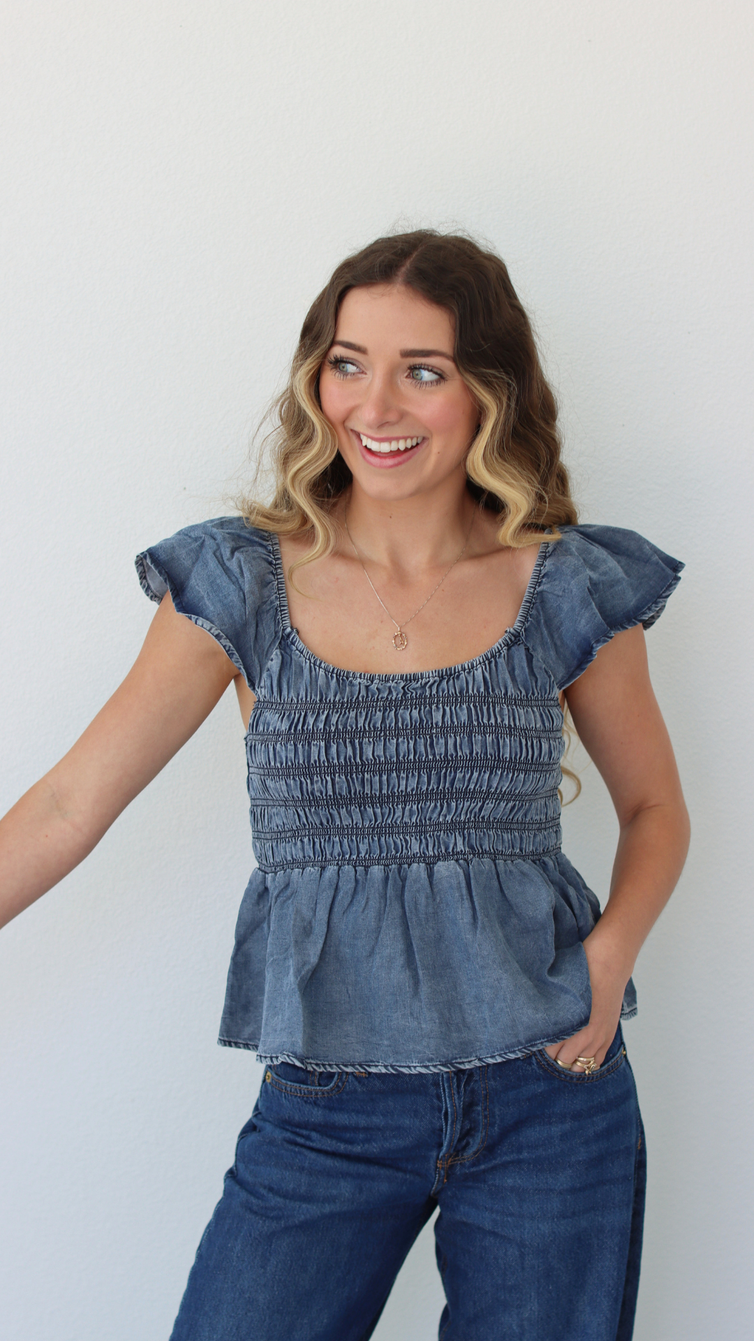 Woman wearing a blue denim top and jeans against a white background