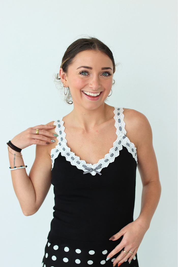 Woman wearing a black top with white lace details against a light blue background