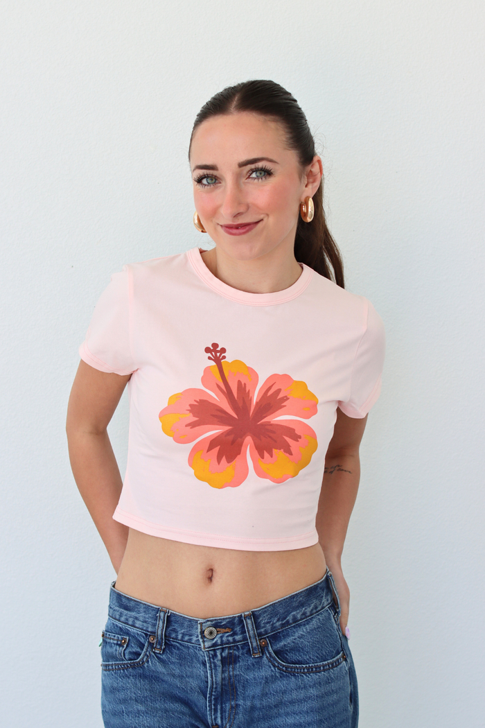 Woman wearing a pink crop top with a floral design against a plain background