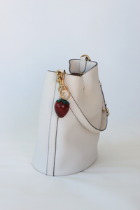 White handbag with a strawberry charm on a white background