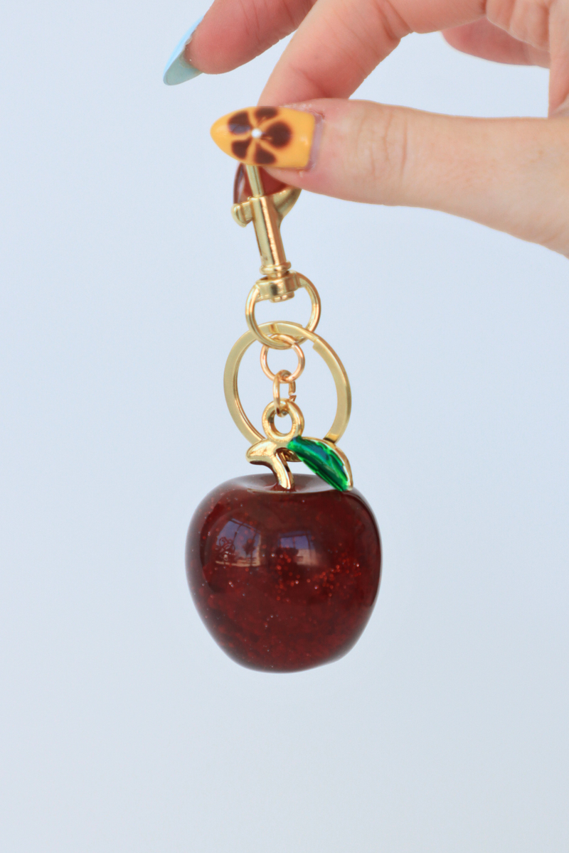 Keychain with a red apple and gold chain on a light blue background