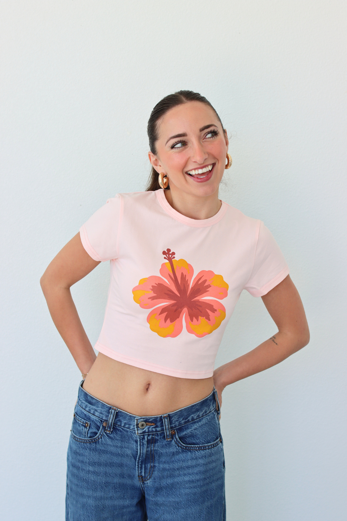 Woman wearing a pink crop top with a floral design and blue jeans against a light background