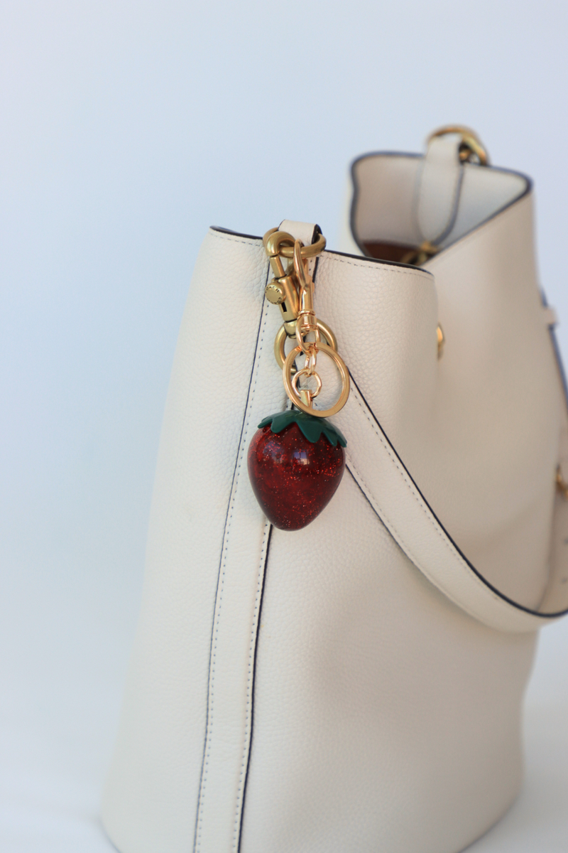 Beige handbag with a strawberry-shaped keychain on a light blue background