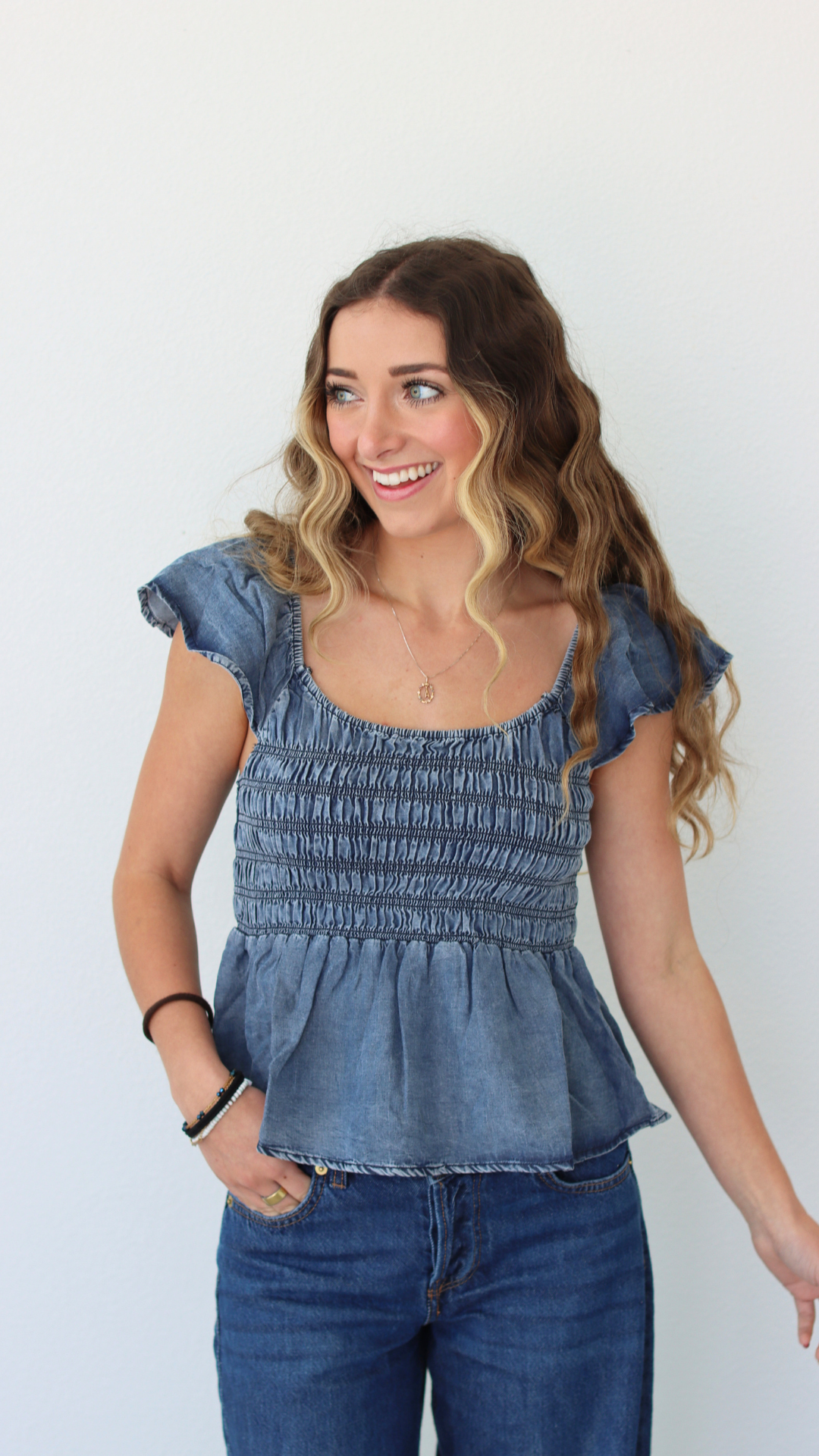 Woman wearing a blue denim top and jeans against a white background