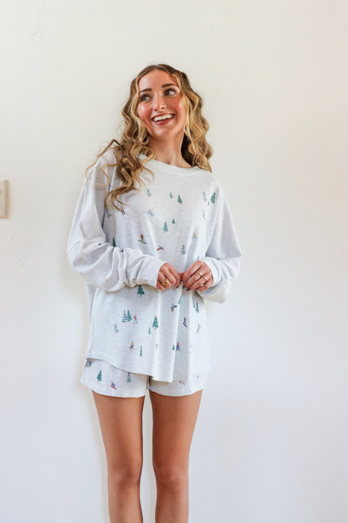 Woman wearing a light gray long-sleeve shirt with a pattern and white shorts against a plain background