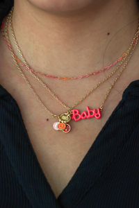 Necklace with 'Baby' charm on a person wearing multiple necklaces.