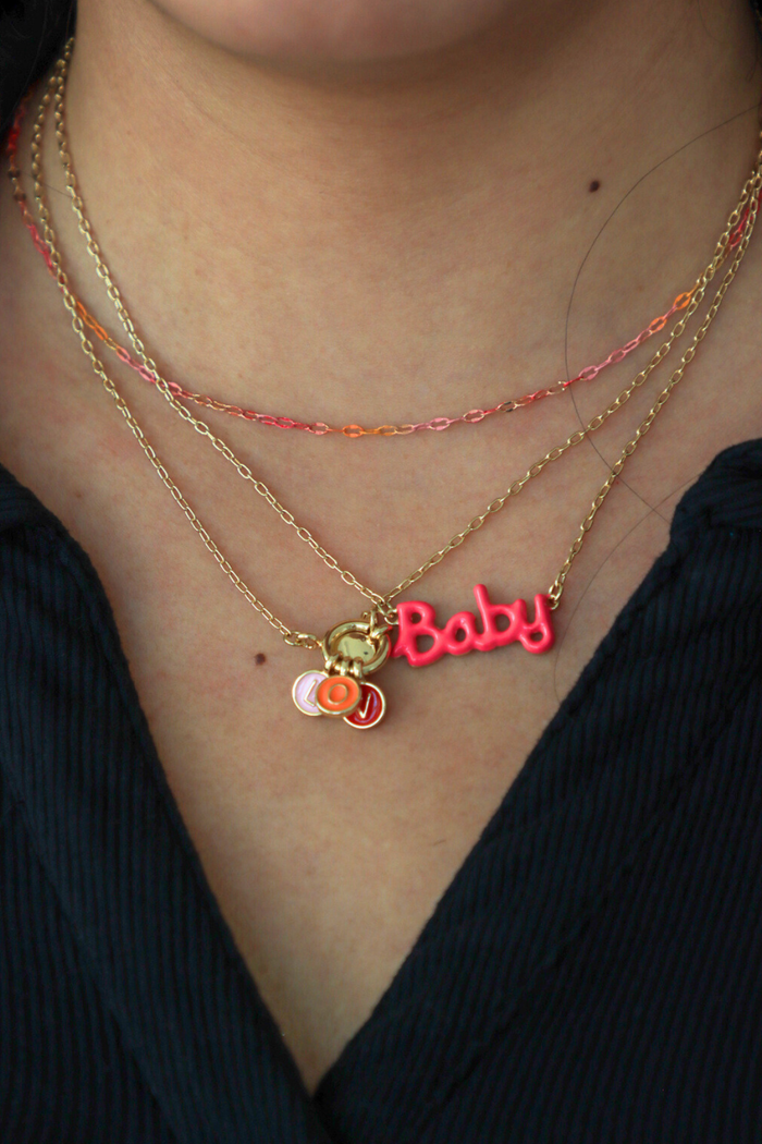 Necklace with 'Baby' charm on a person wearing multiple necklaces.