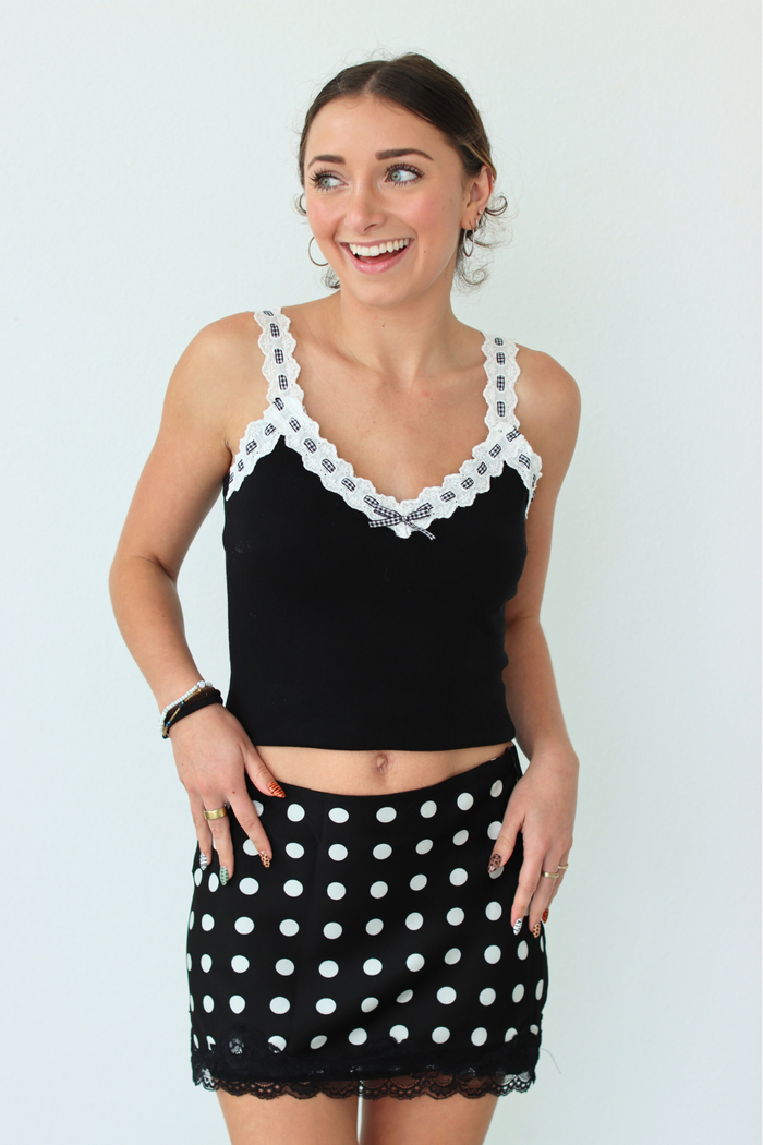 Woman wearing a black top with white lace trim and a black polka dot skirt on a light gray background