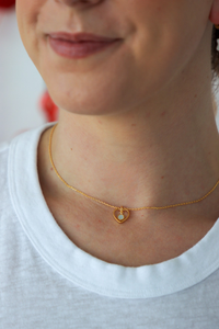 Close-up of a person wearing a gold necklace with a heart-shaped pendant.